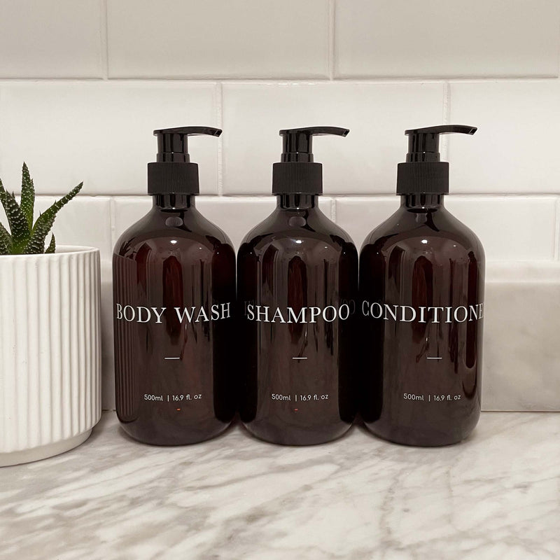 Three brown bathroom pump bottles labeled 'Body Wash', 'Shampoo', and 'Conditioner'. Elegant refillable bathroom bottles with customisable text printed on,
